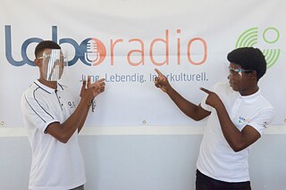 Zwei Jugendliche stehen vor dem Laboradio-Poster und zeigen darauf