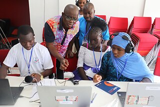 Mehrere Jugendliche mit einem Erwachsenen besprechen sich vor einem Laptop