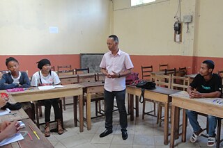Schüler und Schülerinnen sitzen im Klassenzimmer, Lehrkraft steht vor ihnen