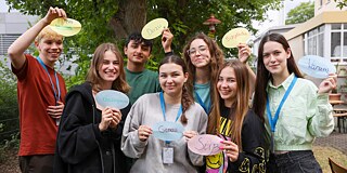 Gruppenbild von sieben Jugendlichen, die ovale Karten mit ihren Lieblingswörtern zeigen.