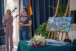 Schülerin steht neben einer Frau im Kostüm vor einem Mikrofon, beide lachen