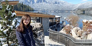 Tritdhamon am Eibsee © privat Frau in dunkler Jacke steht vor vor einer Holzhütte an einem verschneiten Gewässer