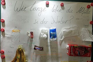 Plakat zu Abfällen in der Schule mit verschiedenen aufgeklebten Beispielen wie einer Bananenschale und Taschentüchern