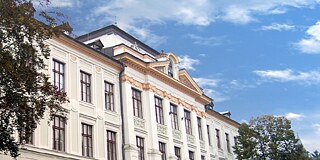 Weißes Schulgebäude mit großen Fenstern, von unten fotografiert