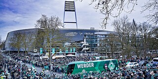 Werder Bremen-Bus auf dem Weg zum Stadion (im Hintergrund), von Menschen umringt