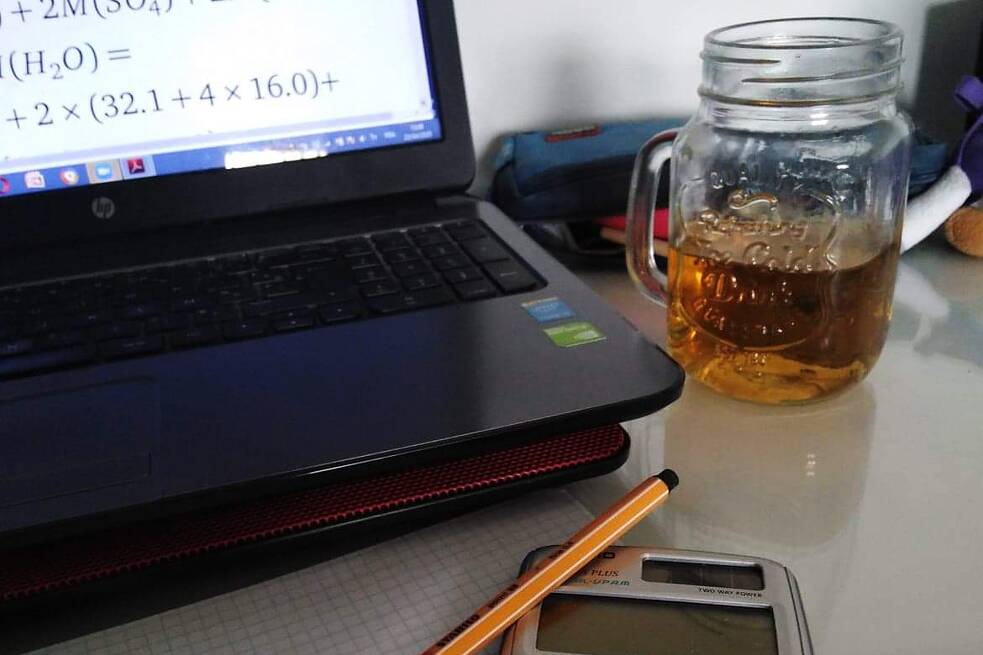 Laptop mit Aufgaben, ein Getränk, ein Taschenrechner und ein Stipft auf einem Tisch