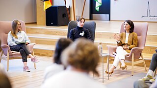 Drei Personen sitzen zusammen auf großen Sesseln vor einem Publikum