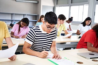 Schülerinnen und Schüler sitzen an Tischen und schauen auf bedrucktes Papier