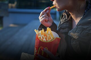 Junge Frau isst Pommes aus der Box einer bekannten Fastfoodkette.