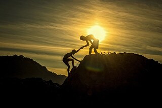 Helfende Hand beim Bergsteigen in der Abenddämmerung