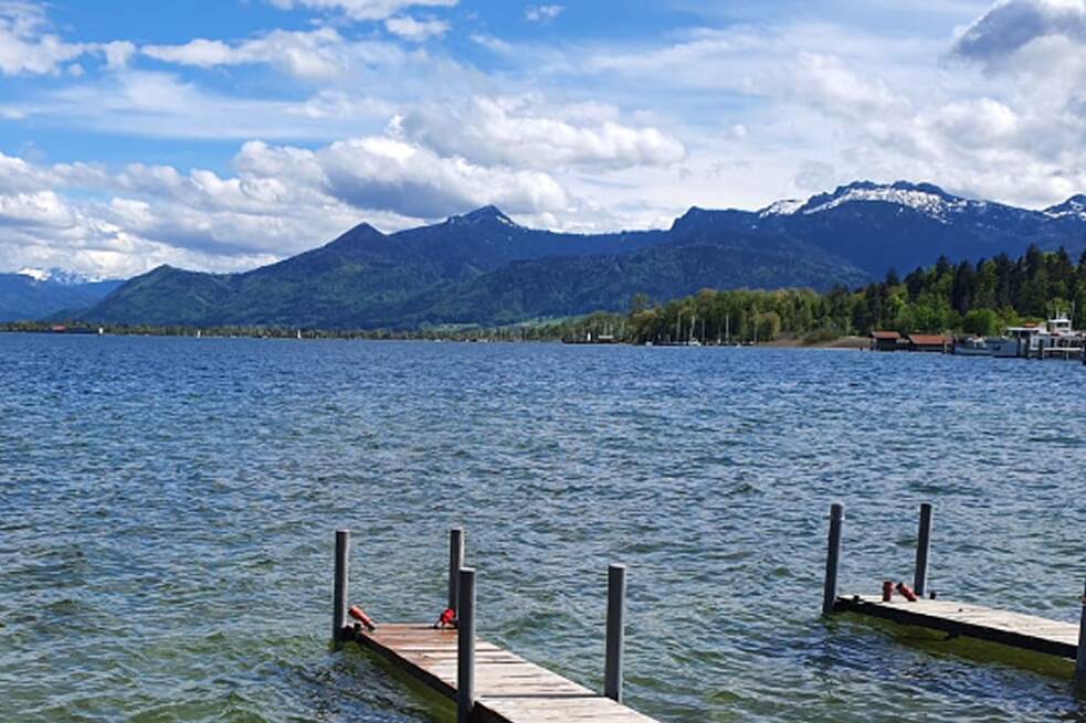 Blick auf einen Steg am Chiemsee, im Hintergrund die Berge