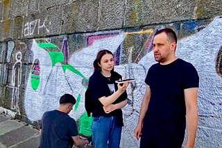 Stimmen aus der Ukraine Drei junge Menschen vor einer mit Grafitti besprühten Wand.