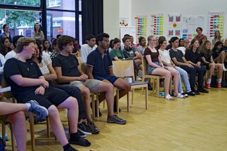 Jugendliche sitzen in einem Halbkreis auf Stühlen und verfolgen eine Darbietung.