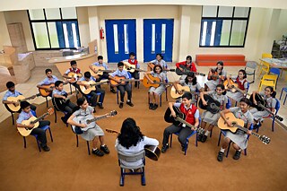 Schülerinnen und Schüler der KLES' International School spielen mit Lehrkraft Gitarre