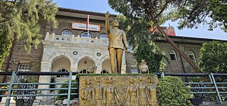 Gebäude, davor Statue und Relief