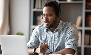 Ein Mann sitzt vor seinem Laptop und sieht konzentriert auf den Bildschirm.