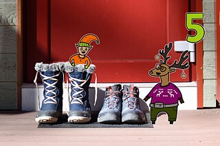 Rentier Matilda und Wichtel Karl stehen lachend vor einer Haustür mit Stiefeln, Karl steckt in einem Stiefel