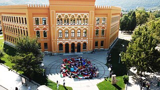 Schülergruppe mit Flaggen vor Schulgebäude