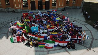 Eine große Gruppe von mindestens 100 Schülerinnen und Schülern mit Flaggen unterschiedlicher Nationen