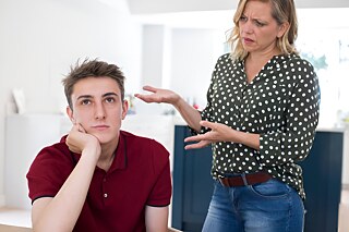 Eine erwachsene, blonde Frau spricht und gestikuliert auf einen gelangweilt Blickenden Jugendlichen ein.