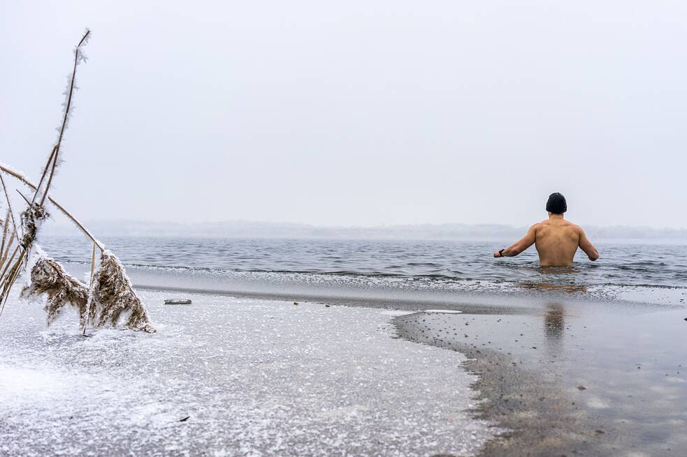 Ein Mann mit nacktem Oberkörper in einem zum Teil zugefrohrenen See.