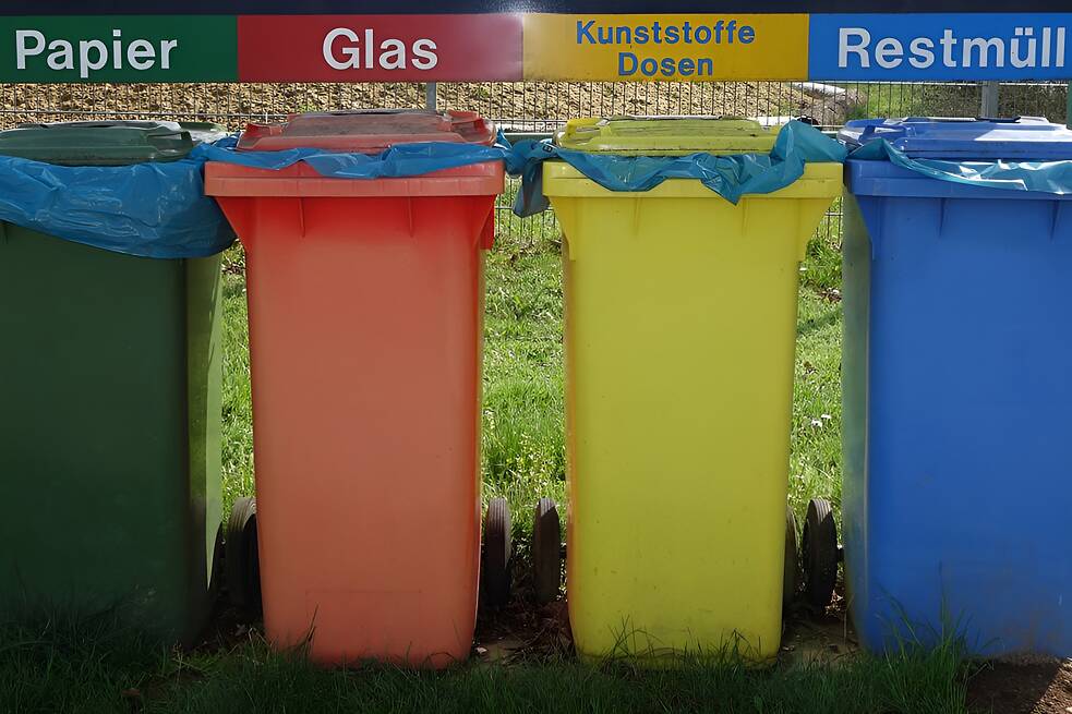 Vier Mülltonnen in den Farben Grün, Rot, Gelb und Blau