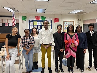 Colson Whitehead steht inmitten einer Gruppe von Schülerinnen und Schüler in einem Klassenzimmer