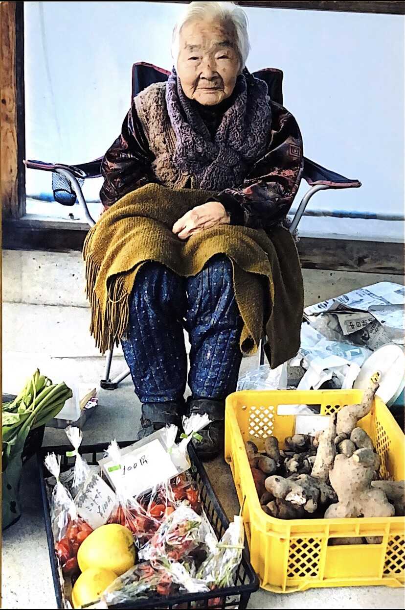 Eine alte japanische Frau verkauft Gemüse auf dem Markt
