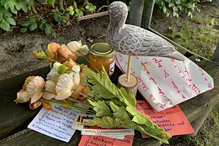 Eine Möve aus Holz, ein Blumenstrauss, mehrere bunte Zettel liegen auf einer Bank