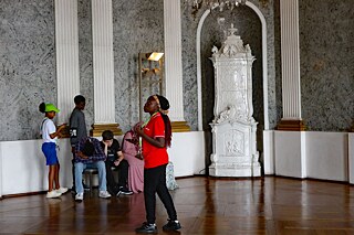 Jugendliche bewundert einen Kronleuchter aus Kristall im Neuen Schloss in Bayreuth. Im Hintergrund ein weißer Kachelofen.