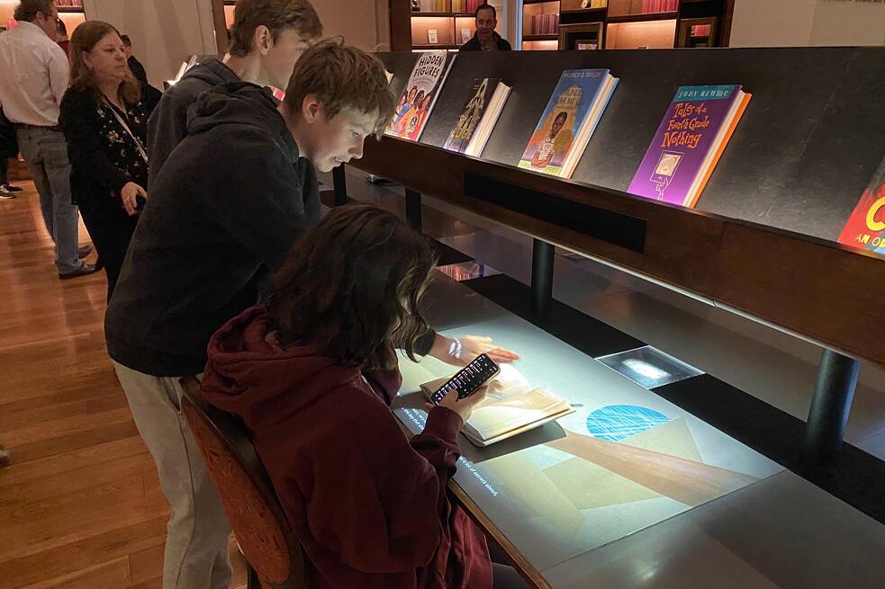 Die Bücherei im Planet Word Museum in Washington D.C. Jugendliche vor einem Pult mit Büchern und elektronischen Geräten in der Schwarzmann Family Library