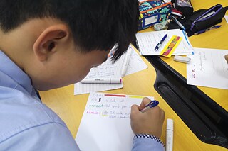 Junger Schüler schreibt einen Text auf Deutsch auf ein Blatt Papier.