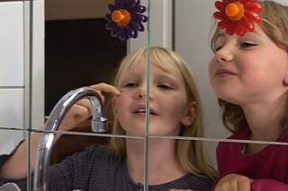 Zwei Mädchen stehen vor dem Badezimmerspiegel und vergleichen ihr Spiegelbild.