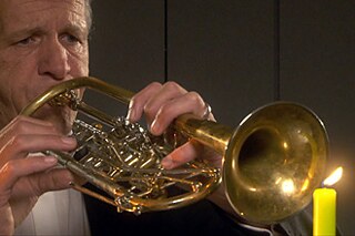 Ein Mann spielt Trompete. Vor der Trompete steht eine brennende Kerze.