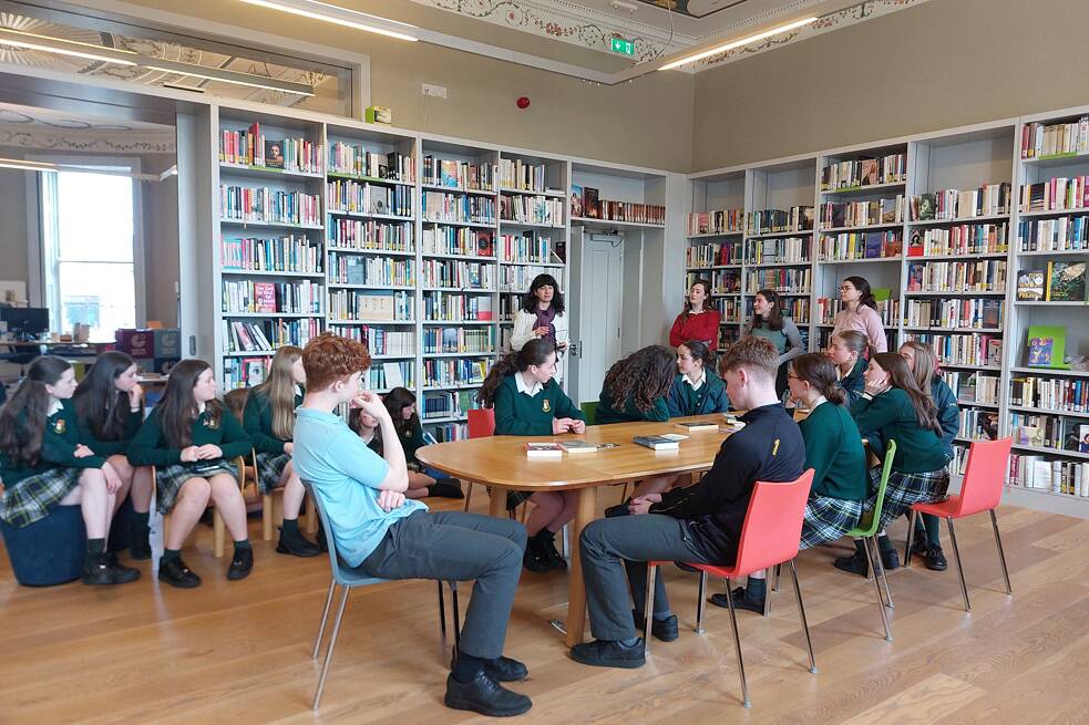 Jugendliche in Schuluniform sitzen an einem großen Tisch in einer Bibliothek.