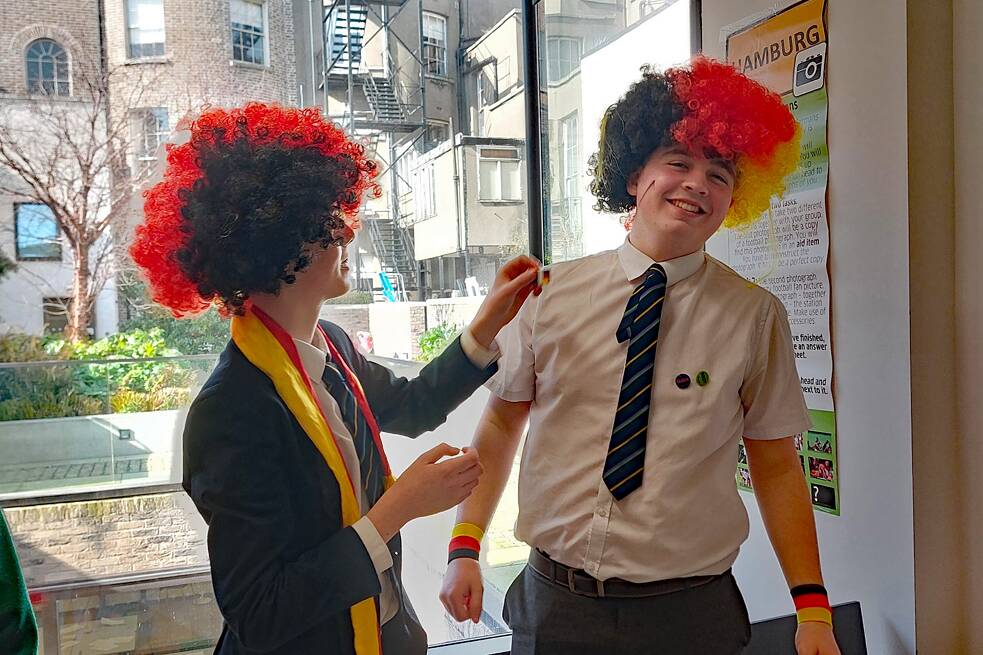 Jugendliche in Schuluniform tragen schwart/rot/goldene Perücken und albern herum.