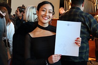 Eine junge Frau zeigt ein Papier mit Logo und Wasserzeichen in die Kamera.