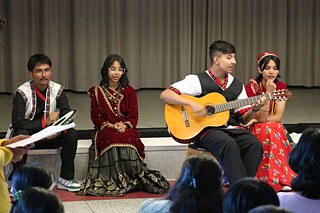 Jugendliche in Landestracht sitzen am Rande einer Bühne, spielen Gitarre und singen