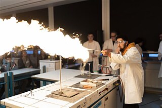 Experimente im Unterricht. In einem Chemielabor führen Schülerinnen und Schuler Experimente durch. Es brennt.