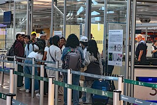 Eine Gruppe Jugendlicher stehen in einer Schlage vor dem Flughafen-Security-Check.