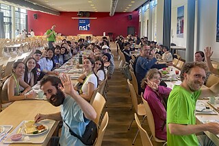 Menschen an langen Tischen bei einer Mahlzeit.