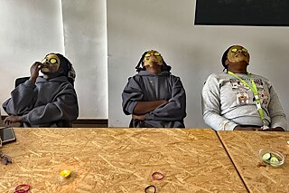 Jugendliche mit Schöneits- und Gurkenmaske sitzen an einem Tisch.