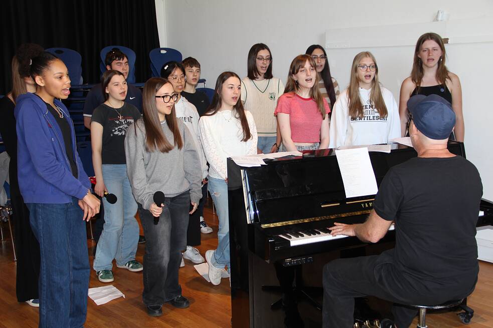 Jugendliche singen, ein Erwachsener spielt auf einem Klavier.