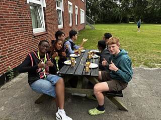Jugendliche sitzen um einen Biertisch und genießen ihr Essen.