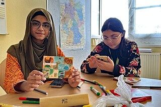 Zwei junge Frauen sitzen an einem Tisch und gestalten Postkarten.