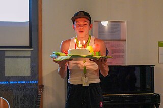 Ein Jugendlicher hält eine Torte und kleine Geschenke in den Händen und bläst die Kerzen auf der Torte aus.