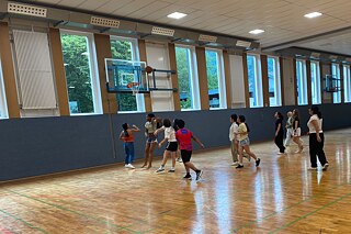 Jugendliche spielen Basketball in einer Sporthalle.