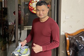 Ein Mann aus China hält Laufschuhe eines bekannten Sportartikelherstellers aus Deutschland in der Hand.