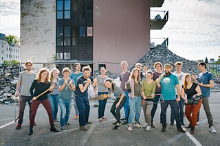 Junge Menschen halten Werkzeug in der Hand und stehen vor einem Gebäude, das renoviert wird.