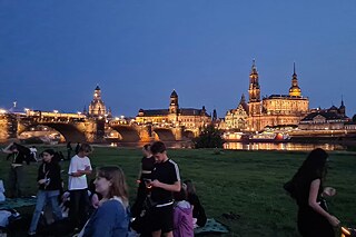 Gruppe Jugendlicher am Ufer der Elbe, im Hintergrund das hell erleuchtete Dresden.